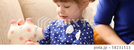 Child little girl arm putting coins into piggybank Child little girl arm putting coins into piggybank 58231513