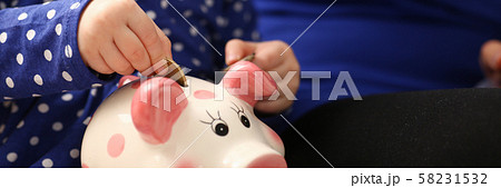 Child little girl arm putting coins into piggybank Child little girl arm putting coins into piggybank 58231532