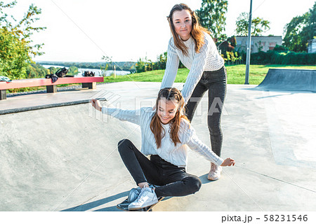 2 teenage girls 14-15 years old, play having fun on skateboard, summer fall spring city, weekend 58231546