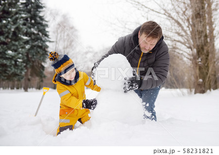 Little boy with his father building snowman in Little boy with his father building snowman in 58231821