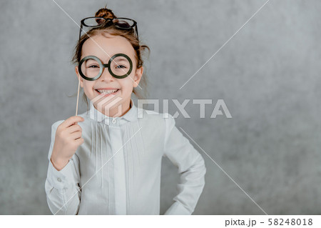 Little business girl on a gray background. During this time, holds cardboard black glasses. 58248018