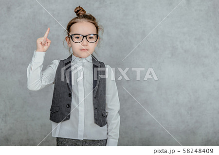 Little business girl is on a gray background. During this time she is dressed in business clothes. Little business girl is on a gray background. During this time she is dressed in business clothes. 58248409