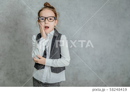 Portrait of a beautiful little girl standing on a gray background. During this surprised look. 58248419