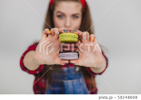 Blurred young pretty woman extending a stack of macaroons to the camera. Focus on macaroons on the 58248608