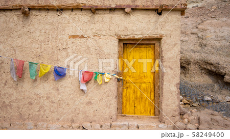 The house built from clay has a yellow entrance door. And there are colorful flags hanging at the front. An old house in the countryside of Leh, India with colorful flags hanging on the wall in front  58249400