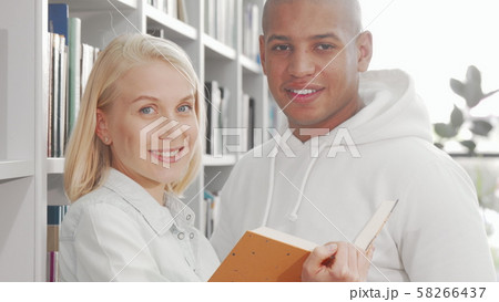 Happy multiethnic couple smiling to the camera while reading a book Happy multiethnic couple smiling to the camera while reading a book 58266437