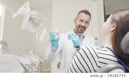 Mature male dentist teaching his patient dental care holding teeth model Mature male dentist teaching his patient dental care holding teeth model 58266743