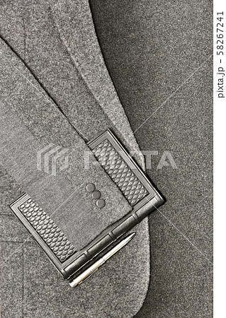 Flat layout business style. Against the background of cloth and a jacket, a leather notebook with a metal pen. In gray shades with a structural surface relief. 58267241