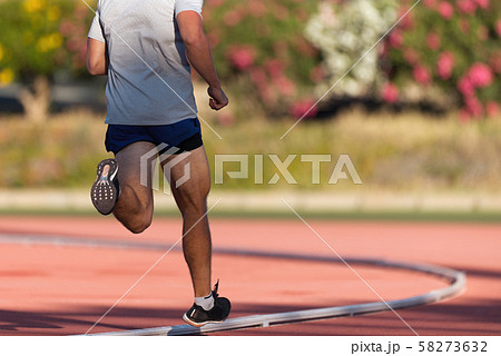 Athlete running and jogging alone along a race track in stadium while out training for competition on a sunny day 58273632