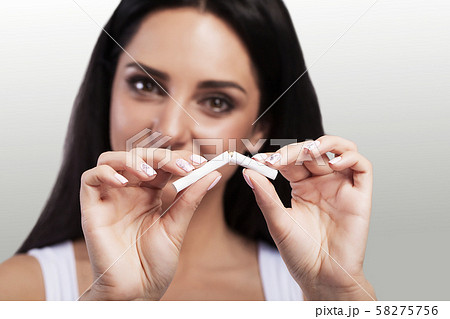 No smoking. A young woman tears a cigarette. Smoking bar. The girl smiles. On a gray background No smoking. A young woman tears a cigarette. Smoking bar. The girl smiles. On a gray background 58275756
