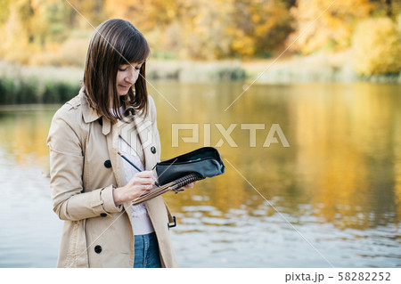 A young girl sketching near a lake in the autumn forest. 58282252