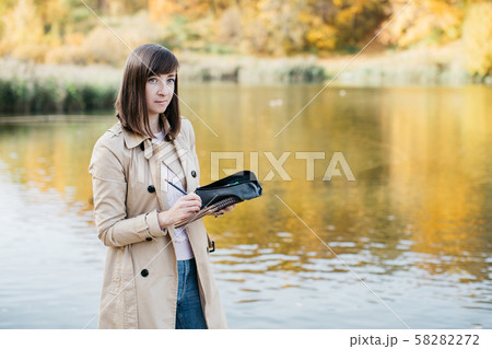 A young girl sketching near a lake in the autumn forest. 58282272