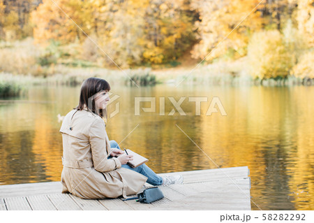 A young girl sketching near a lake in the autumn forest. 58282292