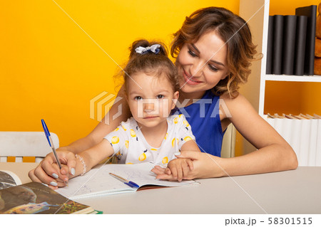 Mother with daughter studying together sitting at the table at home isolated. 58301515