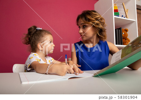 Mother and daughter sitting at the desk doing homework together. Mother and daughter sitting at the desk doing homework together. 58301904
