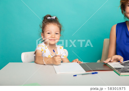 Cute little girl sitting at the desk with pen and mother near. 58301975