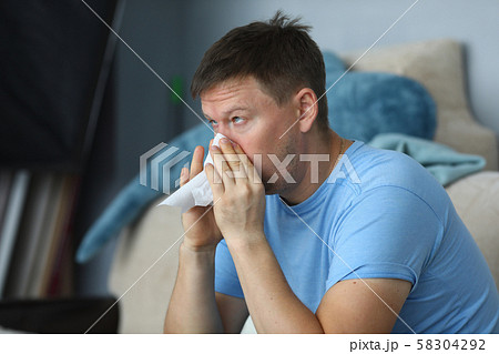 Man blowing his nose in a napkin while sitting 58304292
