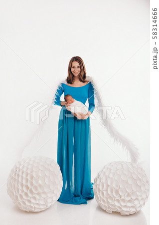 A girl in a blue dress with angel wings holding a newborn baby on a white background. An angel-woman and child have big white balls. The concept of Christmas, mystical creatures, Halloween A girl in a blue dress with angel wings holding a newborn baby on a white background. An angel-woman and child have big white balls. The concept of Christmas, mystical creatures, Halloween 58314666