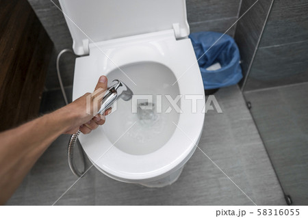 Using of bidet shower with a white toilet. Bidet shower in male hand for using with a white toilet 58316055