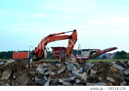 Heavy excavator working at construction site. Unloading stone or concrete waste in mobile crusher  58316126