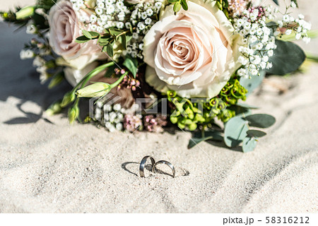 Beautiful wedding rings lie in the sand surface at the beach against the background of a bride 58316212