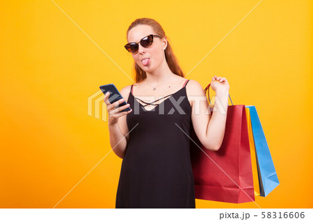 Cheerful young woman wearing sunglasses and holding colorful shopping bags 58316606