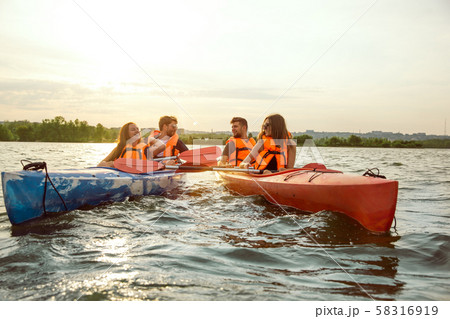 Happy friends kayaking on river with sunset on the background 58316919