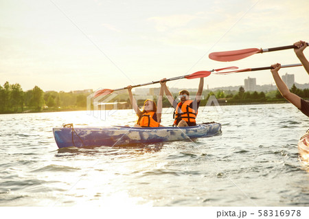 Happy couple kayaking on river with sunset on the background Happy couple kayaking on river with sunset on the background 58316978