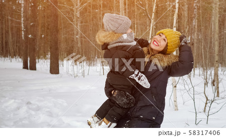 Young mom with little son in her hands is looking at snowfall in winter forest. Young mom with little son in her hands is looking at snowfall in winter forest. 58317406