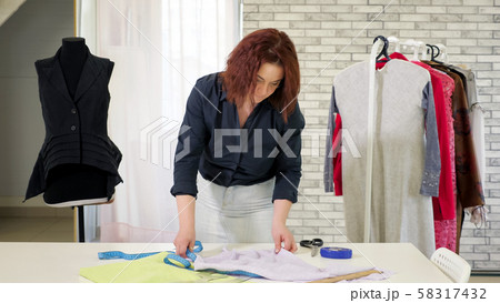 Tailor woman measures cloth use tape on table to make pattern to future clothes. Tailor woman measures cloth use tape on table to make pattern to future clothes. 58317432