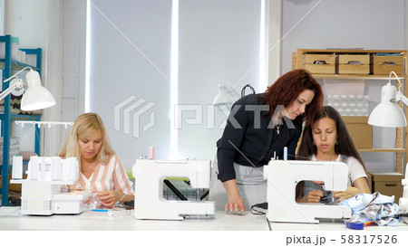 Seamstress teacher teaches her students to sew on sewing machines in workshop. 58317526