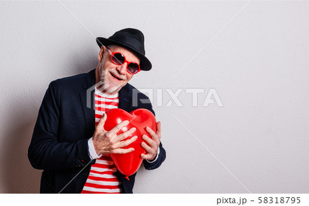 Portrait of a senior man in love in a studio, holding a red heart balloon. Portrait of a senior man in love in a studio, holding a red heart balloon. 58318795