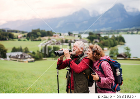 Senior pensioner couple with hiking in nature, using binoculars. 58319257