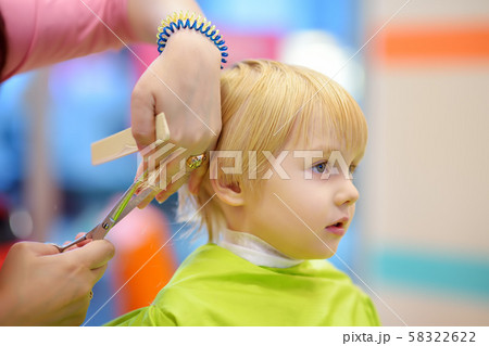 Preschooler boy getting haircut. Children hairdresser with professional tools - comb and scissors. Preschooler boy getting haircut. Children hairdresser with professional tools - comb and scissors. 58322622