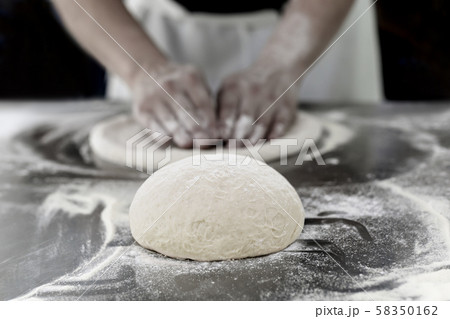 Ball of pizza dough on table with chef hands knead the dough in background. 58350162