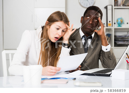 Unhappy managers working with laptop and documents at table in office Unhappy managers working with laptop and documents at table in office 58366859