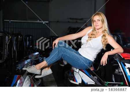 Cheerful young caucasian woman near racing cars at kart circuit 58366887