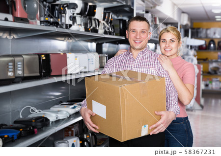 Happy young family holding packed purchases in appliances store Happy young family holding packed purchases in appliances store 58367231