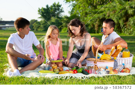 Happy young parents with two teenagers having a picnic on the countryside Happy young parents with two teenagers having a picnic on the countryside 58367572