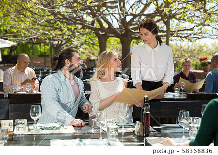 Charming young waiter and couple at open-air restaurant summer Charming young waiter and couple at open-air restaurant summer 58368836