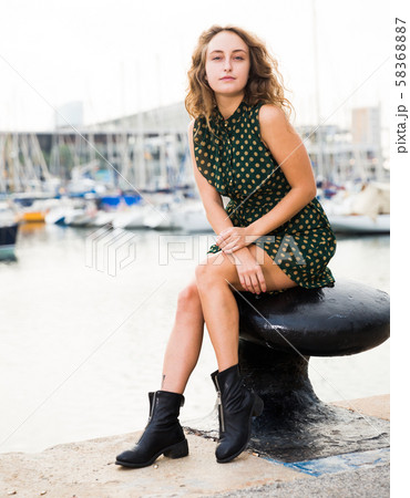 Young girl tourist in dress sitting at stone bench in port with boats Young girl tourist in dress sitting at stone bench in port with boats 58368887