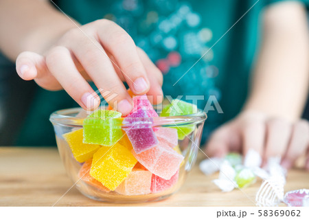 Closeup hands of a little child taking a piece of jelly cube with sugar in a glass bowl. Snacks time, Sugary treats, Party, Kids favorite, Unhealthy, Cavity, Sugar addiction, School, Home, Sweetness. 58369062