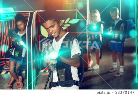 Emotional afro-american boy with laser pistol playing laser tag with friends on dark labyrinth 58370147