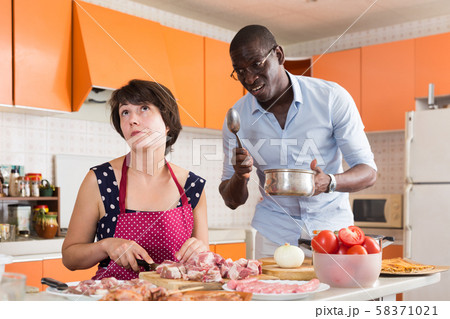 Bored woman cooking with displeased husband Bored woman cooking with displeased husband 58371021