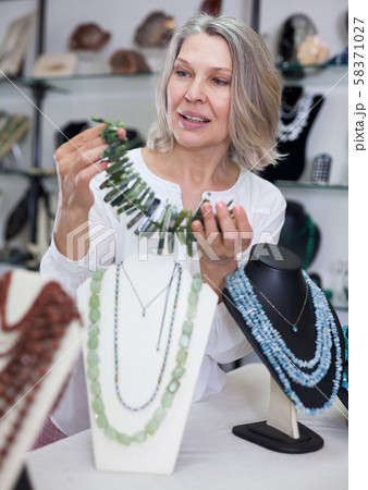 Adult woman chooses jewelry from turquoise and amber jewelery in the store Adult woman chooses jewelry from turquoise and amber jewelery in the store 58371027