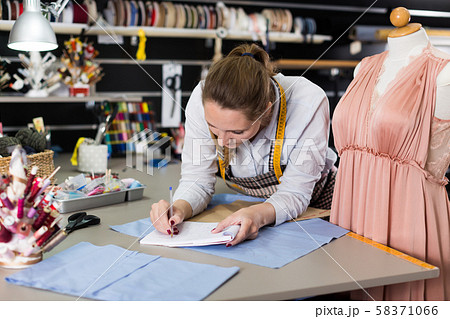 Woman professional sewer writing information about measuring textile Woman professional sewer writing information about measuring textile 58371066
