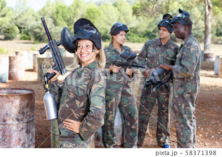 Young woman wearing uniform and holding gun ready for playing paintball with friends outdoor Young woman wearing uniform and holding gun ready for playing paintball with friends outdoor 58371398