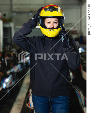 Cheerful young woman in yellow helmet at kart circuit 58372130