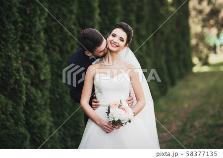 Stylish couple of happy newlyweds walking in the park on their wedding day with bouquet 58377135