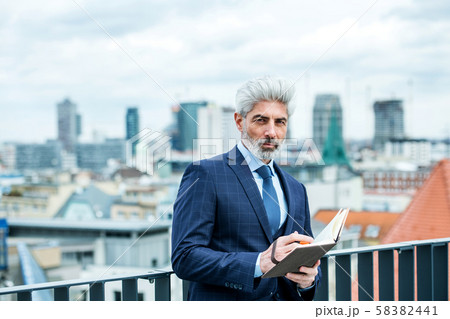 A mature businessman with diary standing on a terrace, writing. A mature businessman with diary standing on a terrace, writing. 58382441